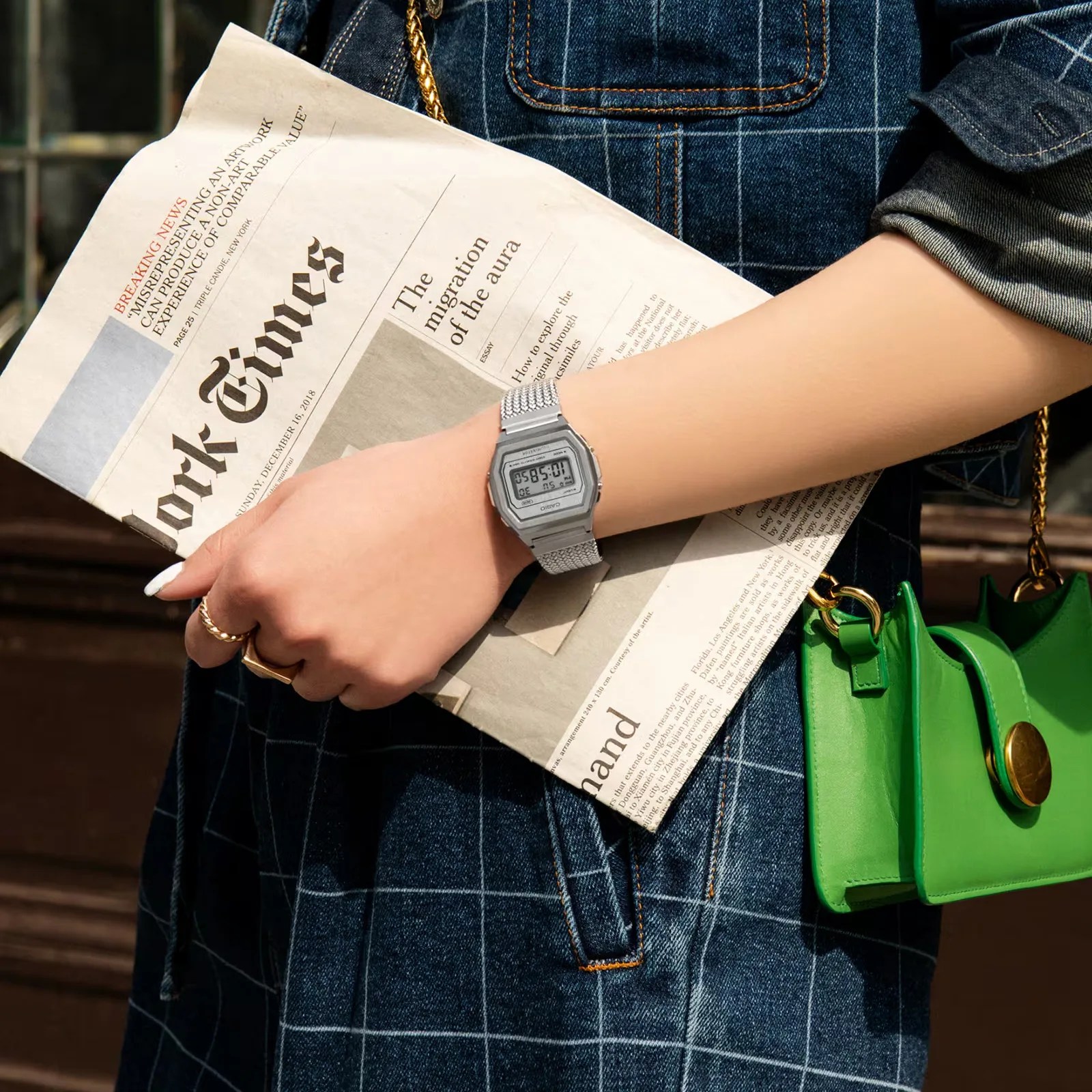 A Casio A1000MA-7VT worn on a woman holding a copy of the New York Times against her checked navy dress