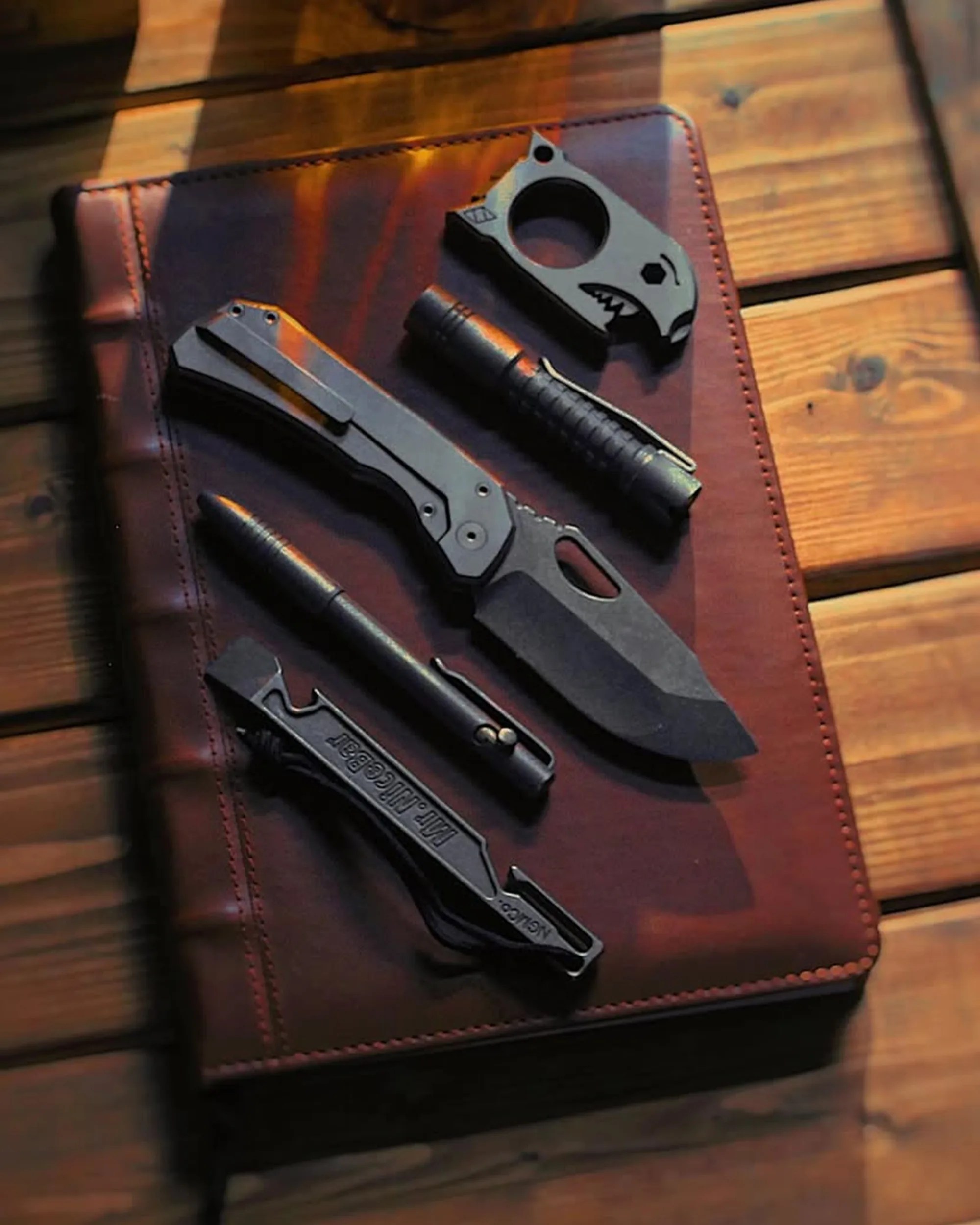 Deadman Design Co Elixir EDC Knife with other EDC gear on leather notebook on wood table