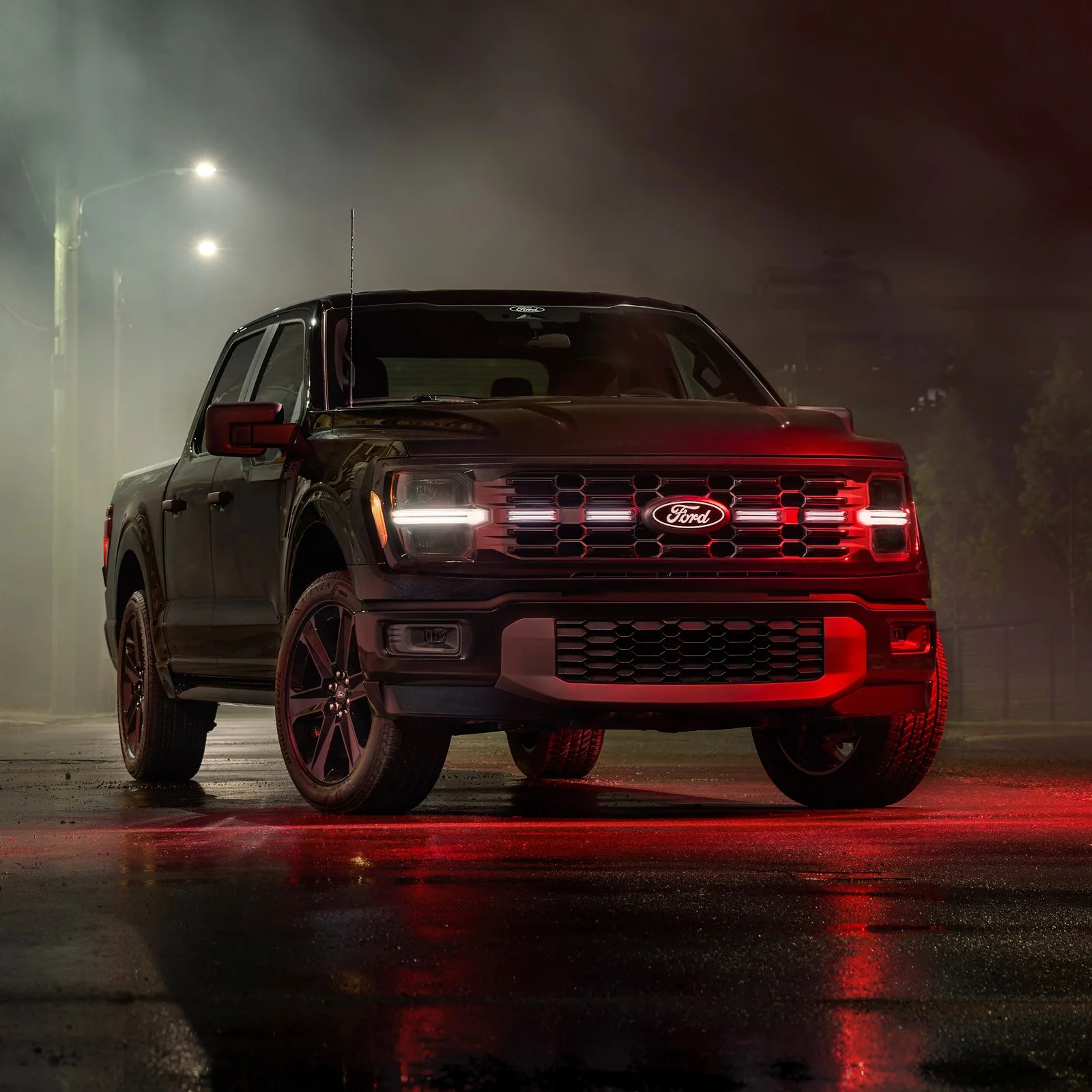 A front view of the 2025 Ford F-150 Lobo with its tail lights on sitting on a foggy street in front of an industrial building