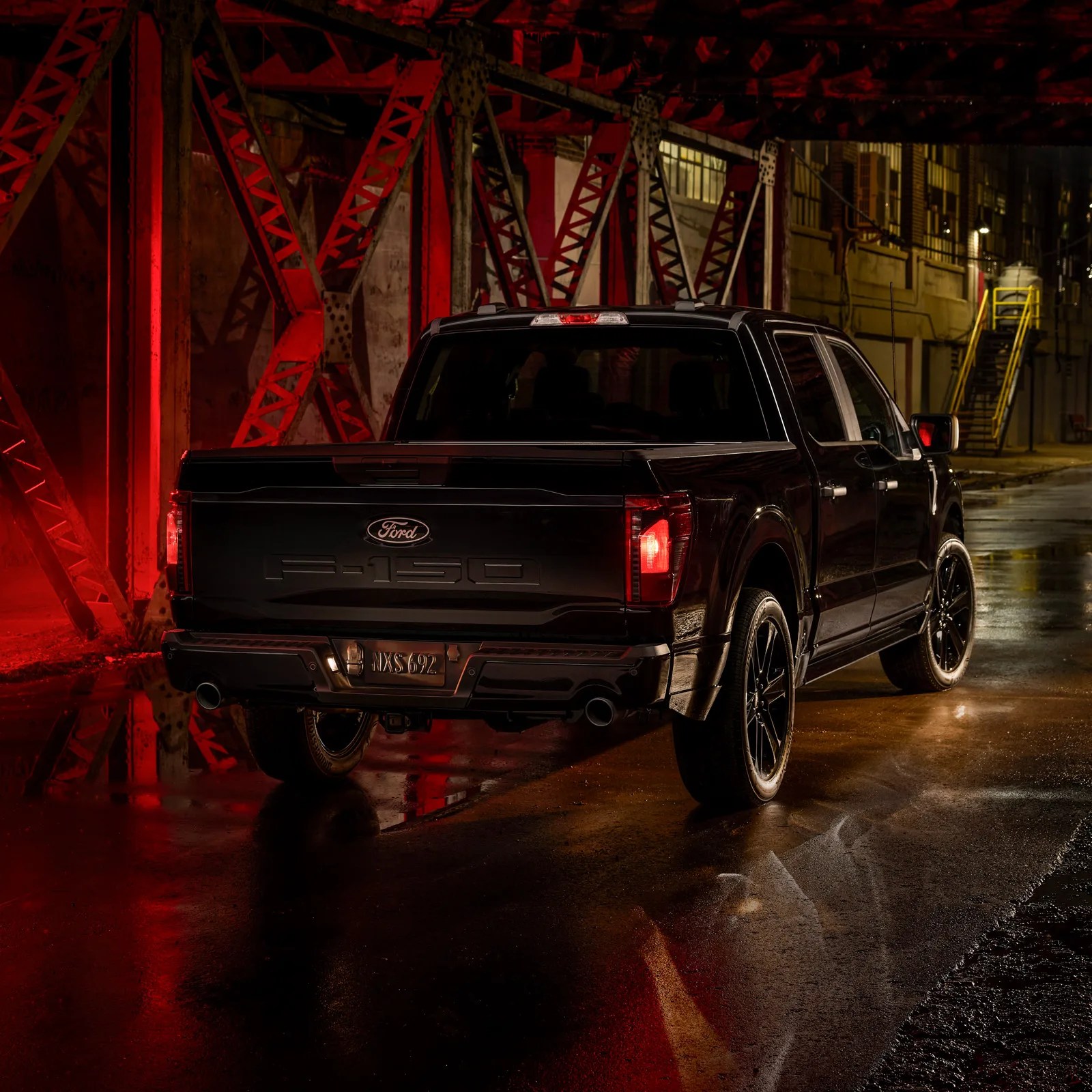 A view of the left rear corner and body of the 2025 Ford F-150 Lobo with the tail lights lit in a warehouse alley