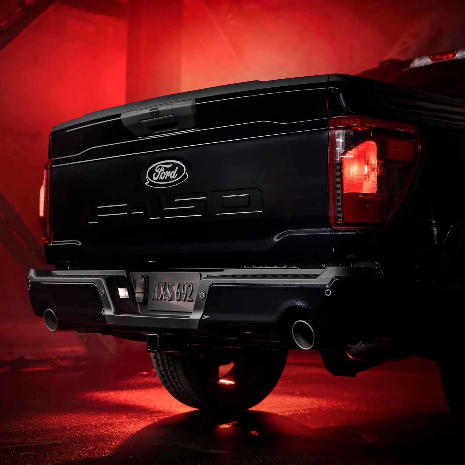 The tailgate and tail lights of the 2025 Ford F-150 Lobo shown backlit in a red light in a warehouse setting.