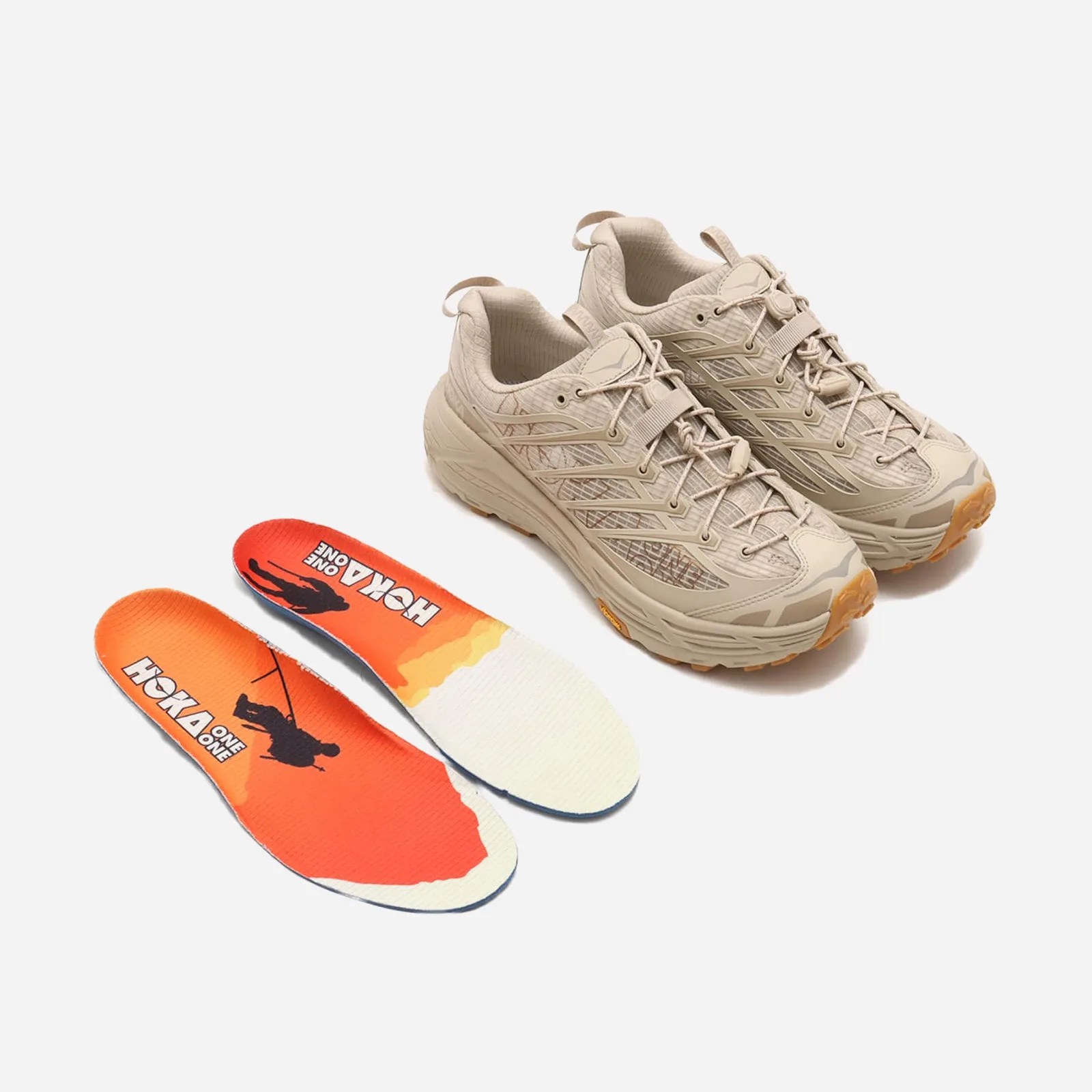 A pair of Hoka Mafate Three2 Grid JP in "Raw Linen / Sand" sitting next to a pair of Hoka insoles. 