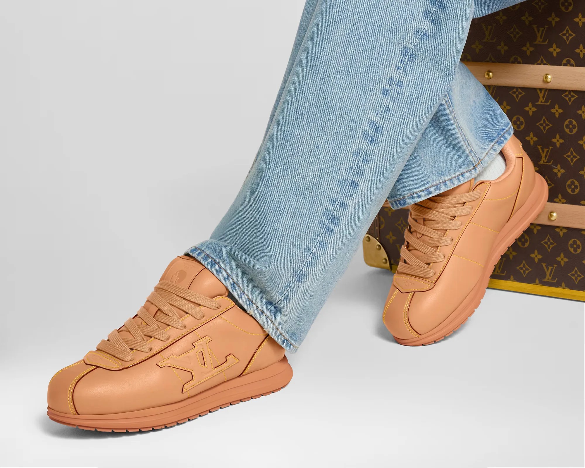 Louis Vuitton LV Buttersoft Sneaker on person in jeans in front of LV luggage