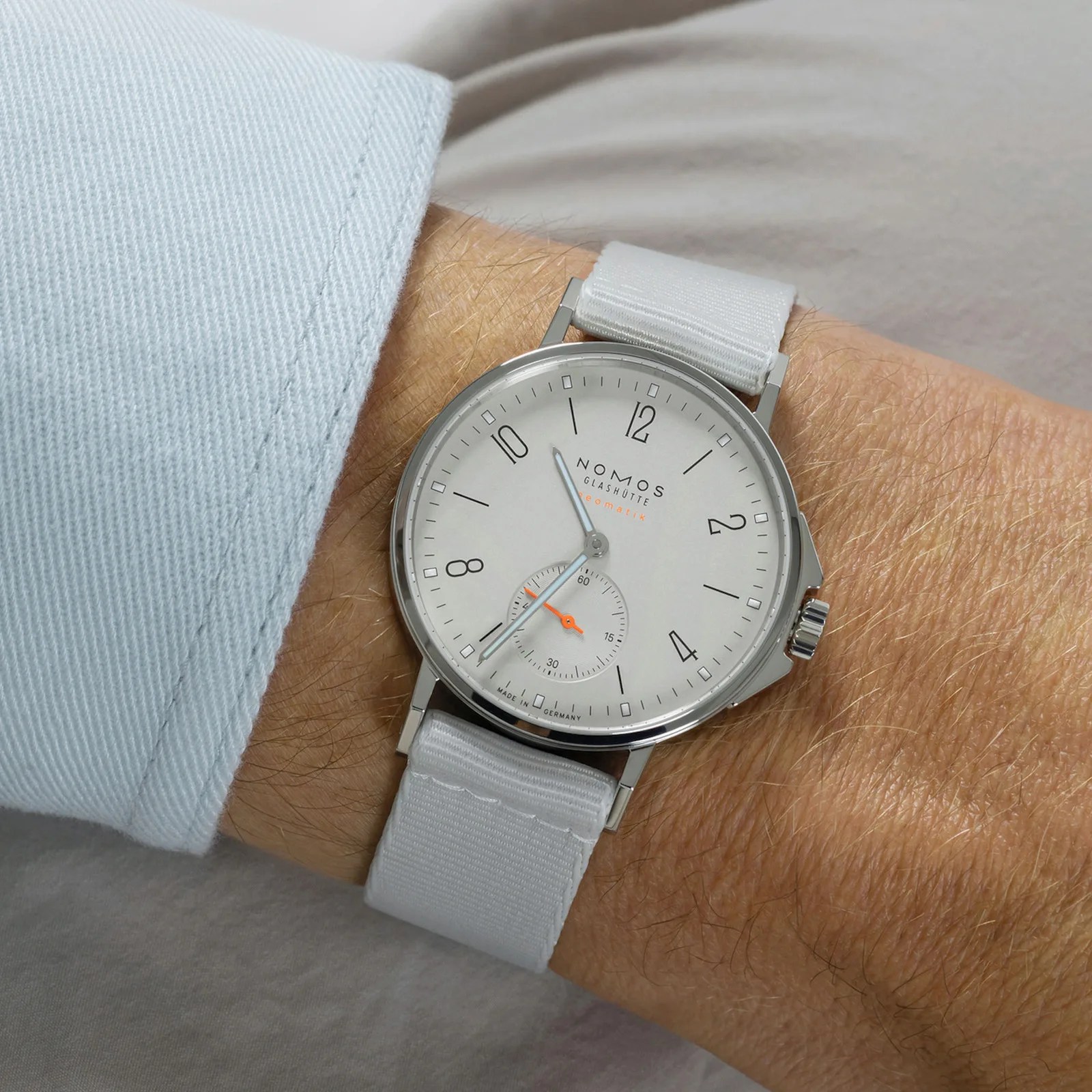 A close-up of the wrist of a man wearing the Nomos Glashütte Ahoi Neomatik Ref 560 in White on his wrist. The cuff of his light blue shirt is visible