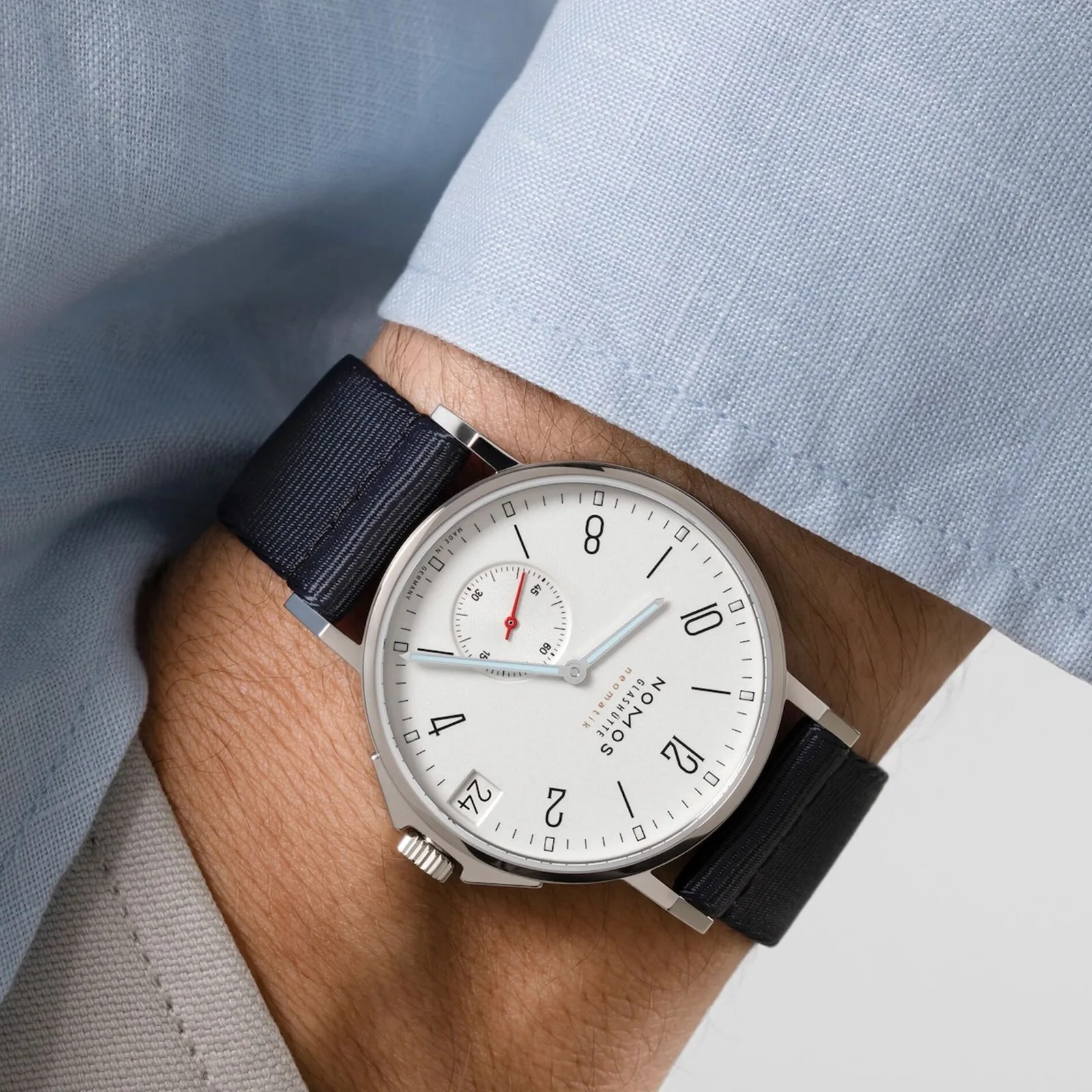 A close-up of the wrist of a man wearing the Nomos Glashütte Ahoi Neomatik 38 Date in White on his wrist. The cuff of his light blue shirt is visible and his hand is stuffed into his pocket.