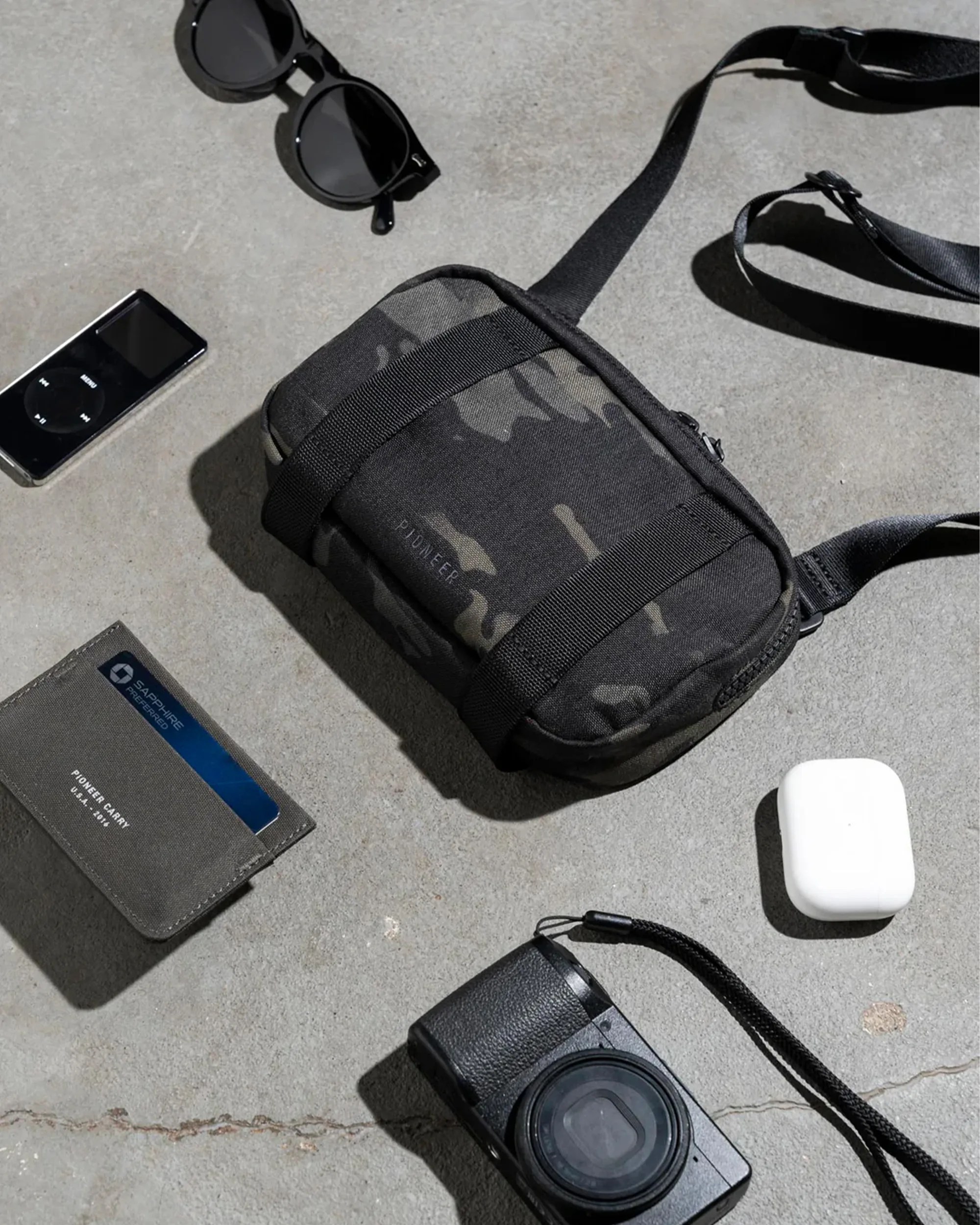 Pioneer Carry Safari EDC Sling bag surrounded by wallet, iPod, AirPods, camera, glasses