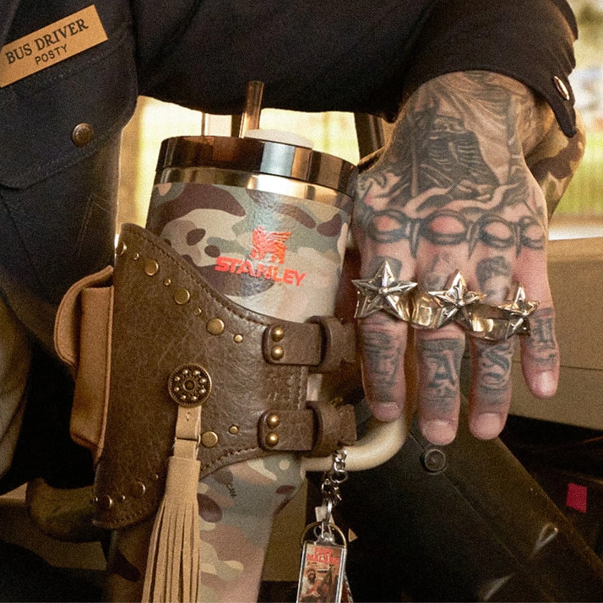 Post Malone x Stanley Quencher H2.0 FlowState Tumbler with Quencher Pouch Belt next to tattooed hand on school bus
