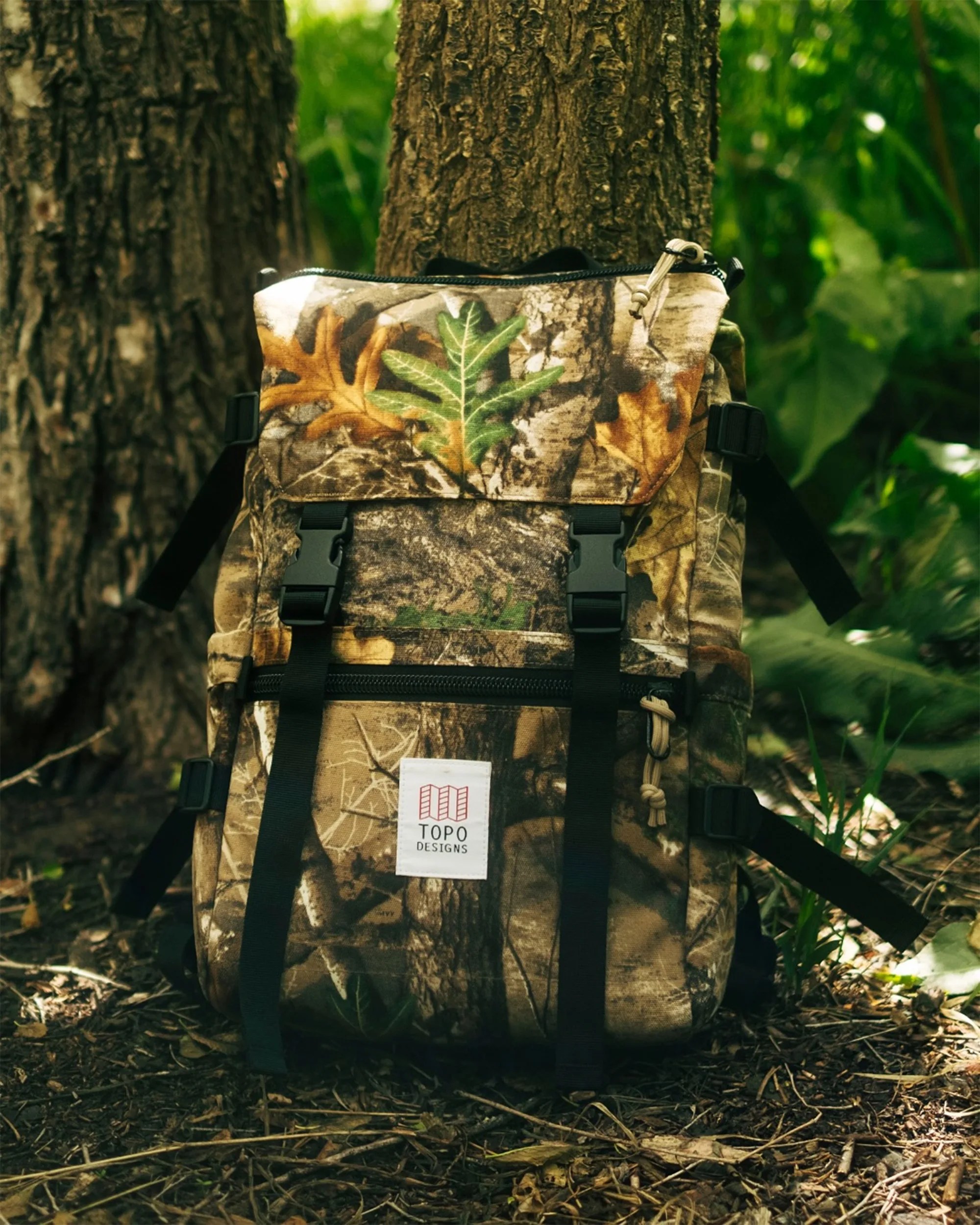 Topo Designs Forest Floor Camo backpack against a tree