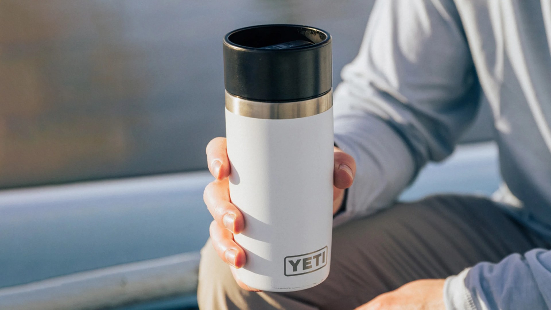 A hand holding a white Yeti Travel mug while sitting on a boat
