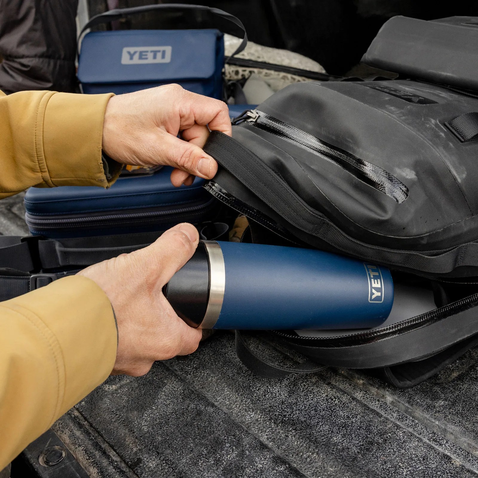 A navy blue Yeti Travel bottle shown being slid into a back pack by a pair of male hands