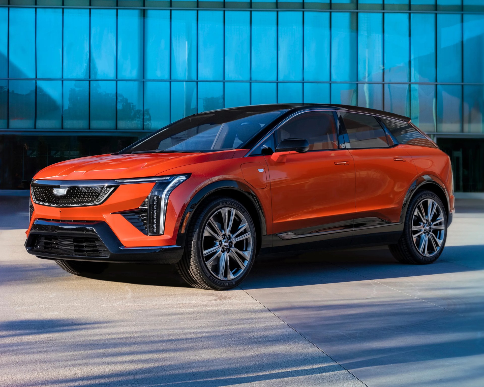 orange cadillac EV parked in front of glass building