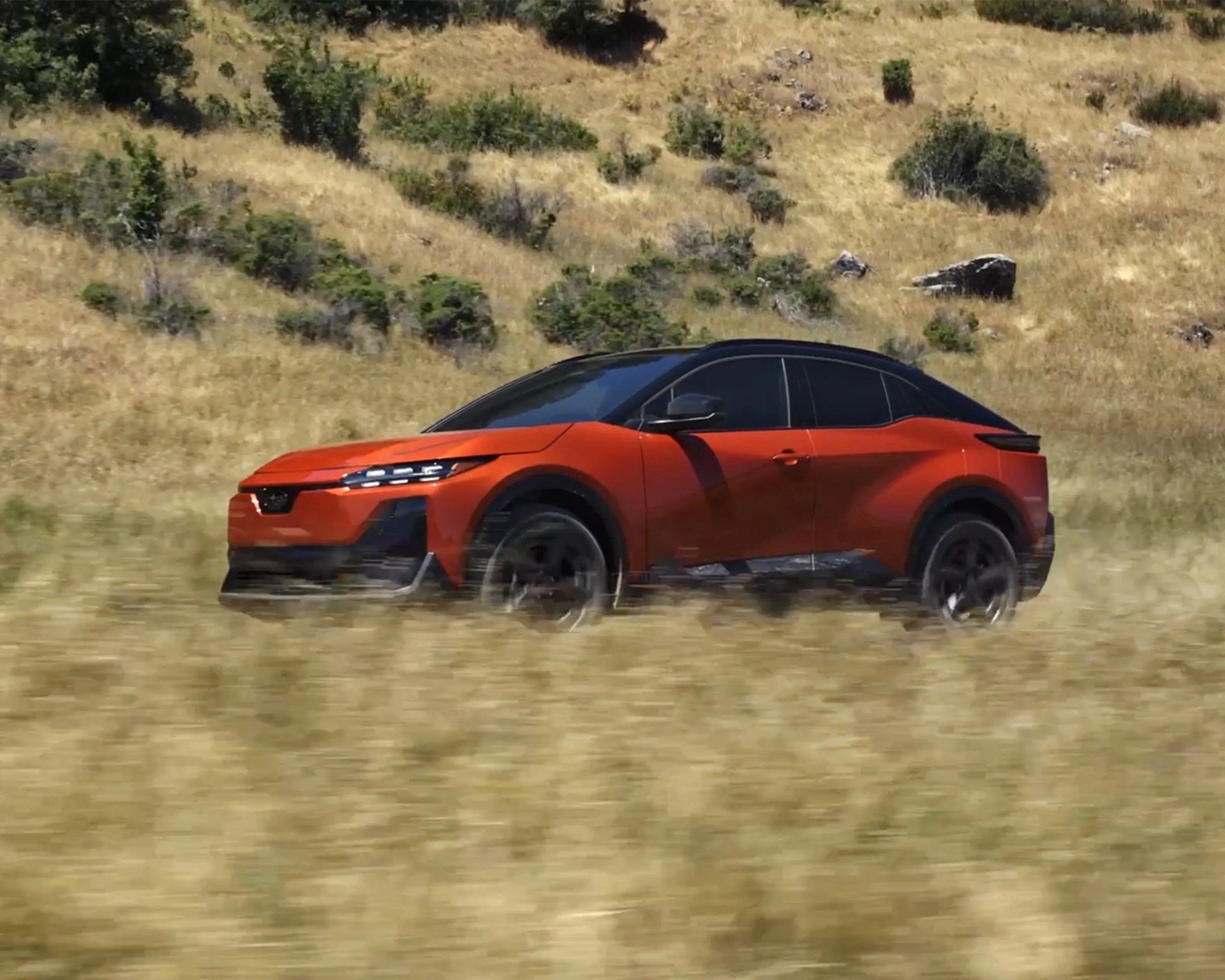 orange subaru electric crossover driving grass