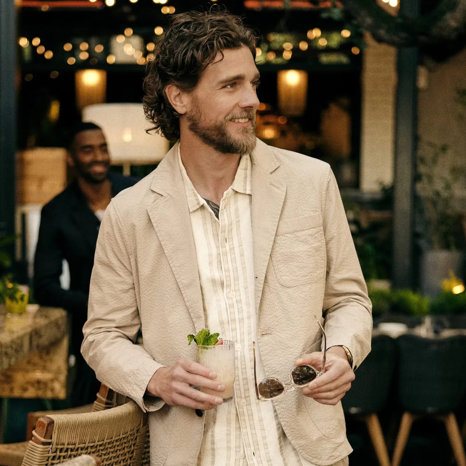The Flint and Tinder Seersucker Blazer in Kahki being shown worn by a male model wearing a white shirt looking to the right holding sunglasses