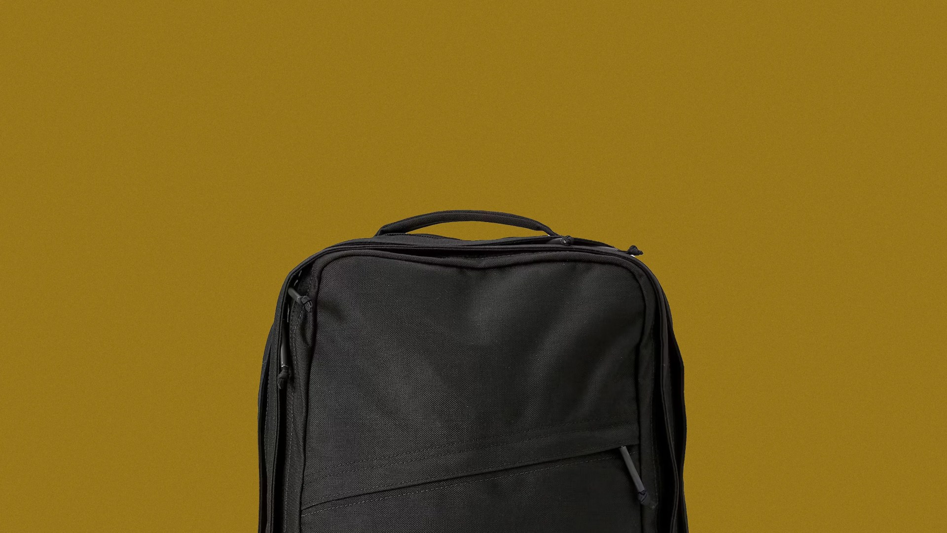 The top portion of the Huckberry x GoRuck GR2 Slick Backpack against a mustard yellow background.