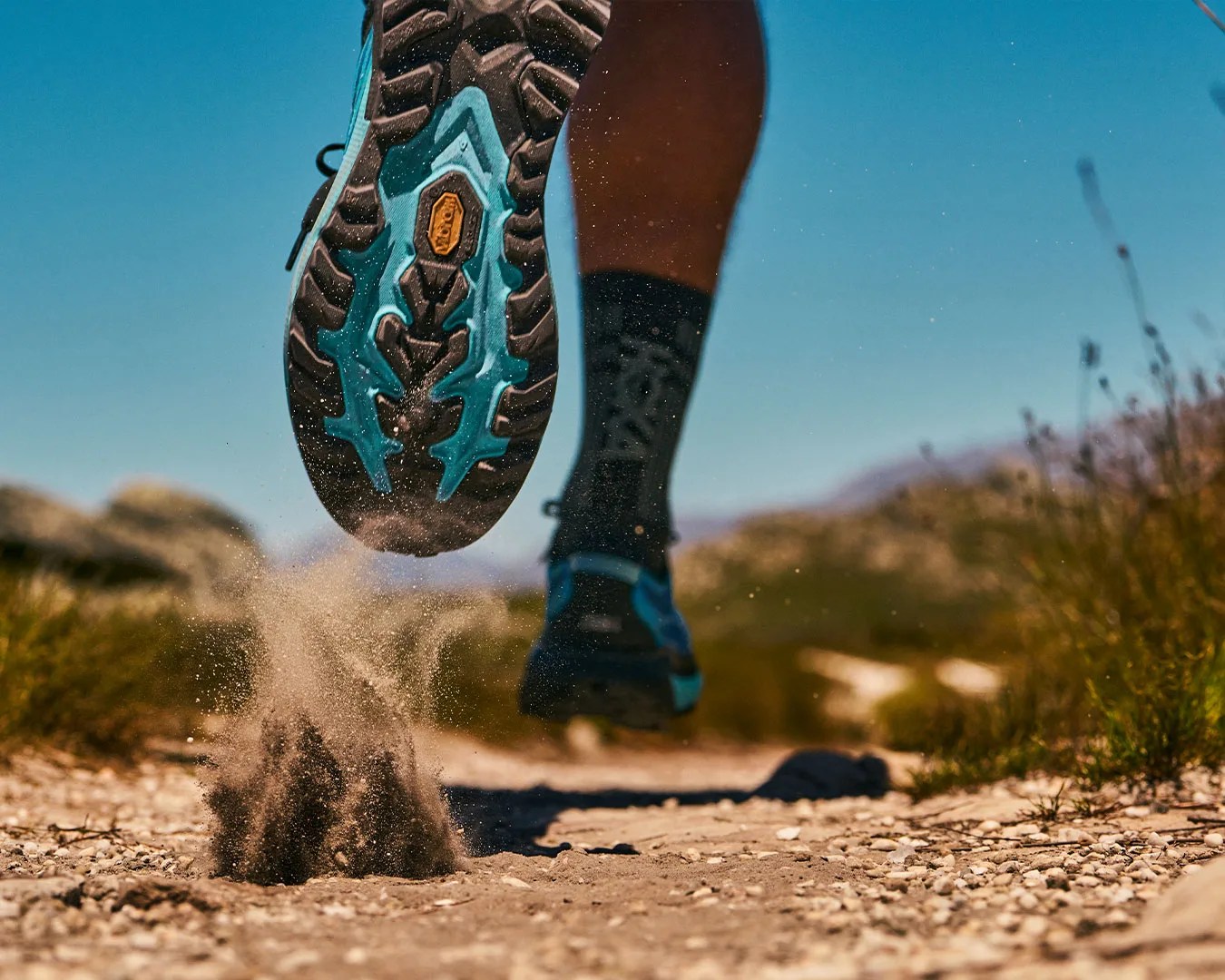 runner wearing Mafate 5 sneaker with a grippy outsole kicking up dirt on path
