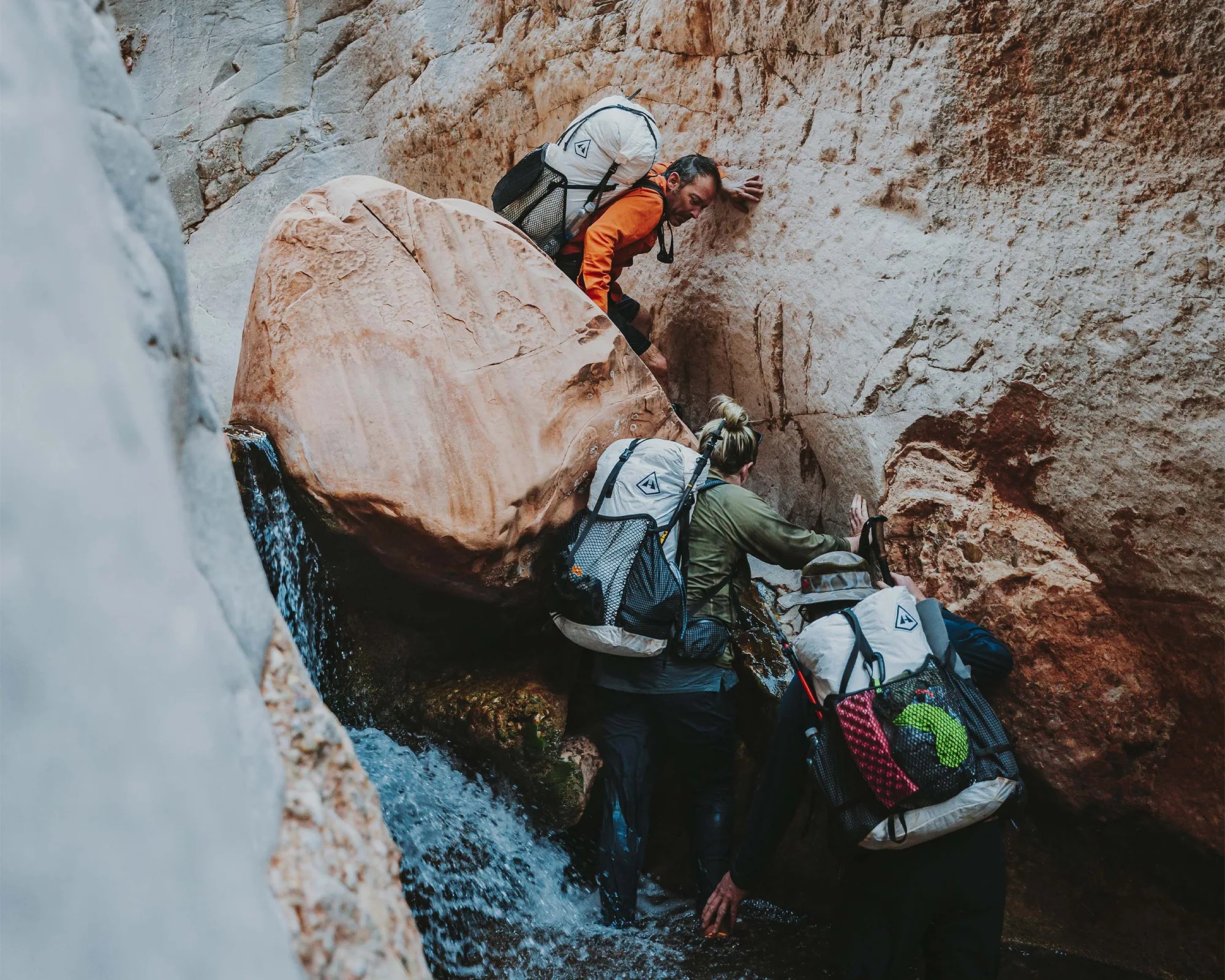 Three hikers fording canyon river wearing Hyperlite Mountain Gear Dyneema Packs