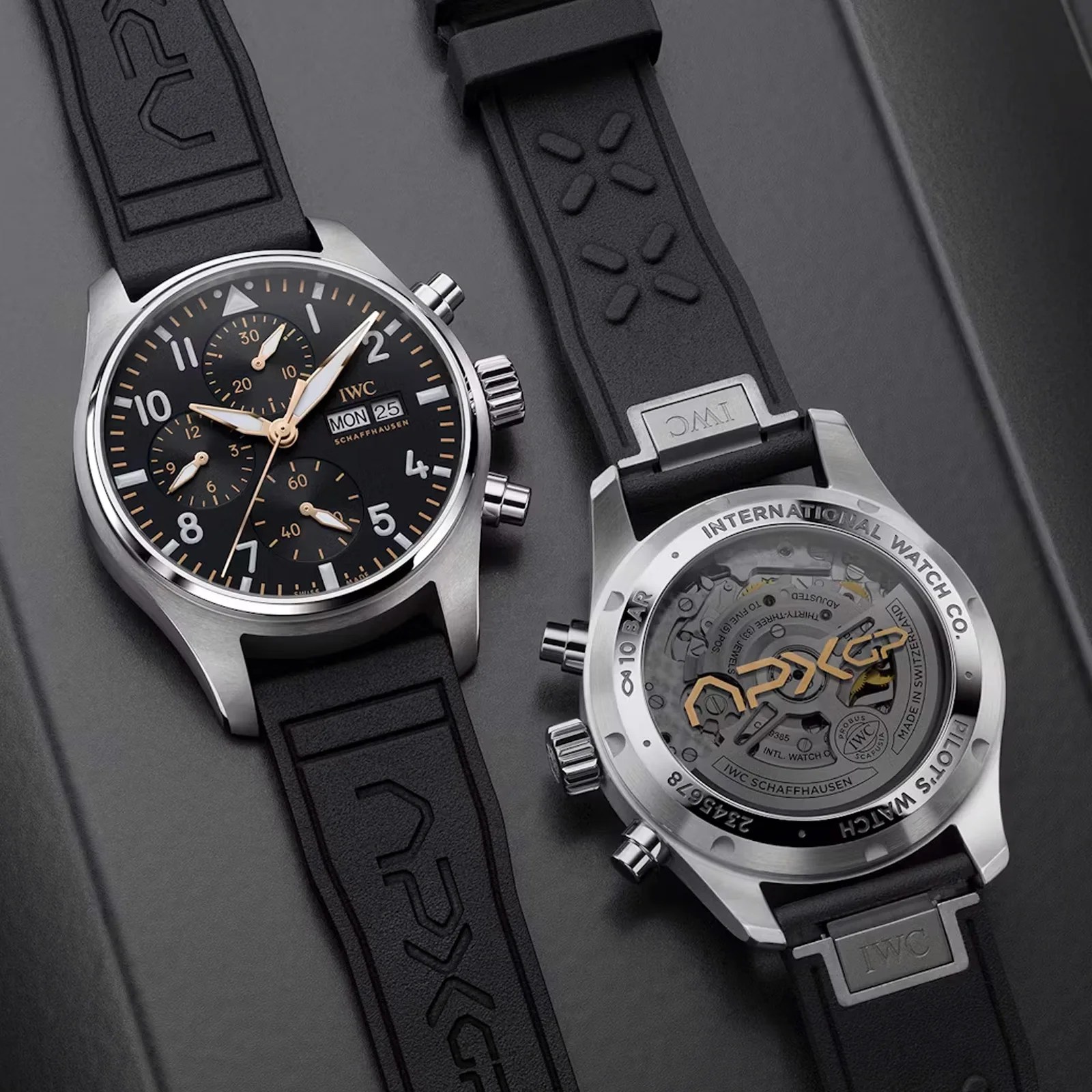 Two IWC Pilot’s Watch Chronograph 41 APXGP's shown laying flat on a grey surface. One is shown face up, the other is face down. Both watches are lying at a diagonal angle as framed in the image