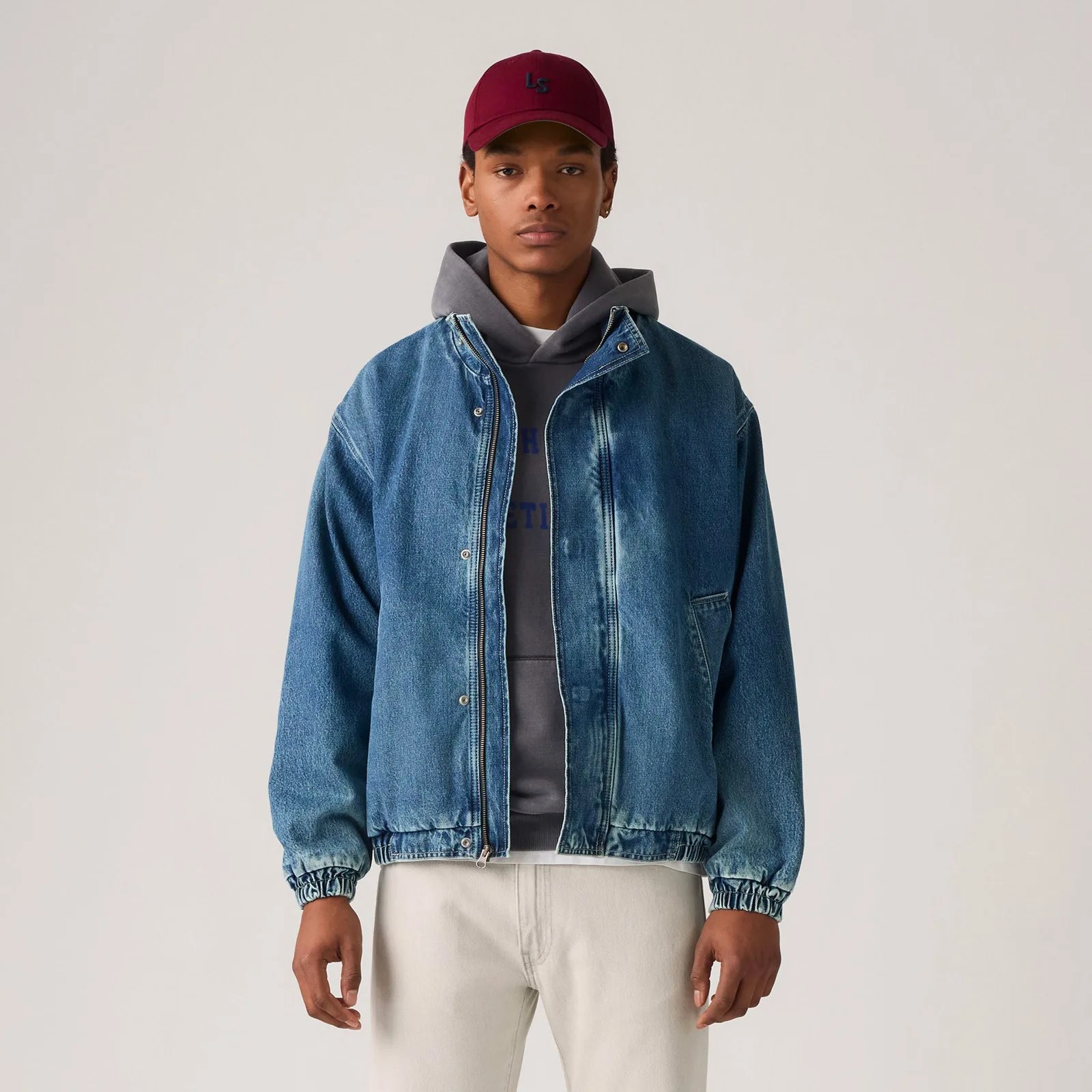 A male model is shown wearing the Levi's Highland Park Denim Jacket over a hooded sweatshirt with his arms hanging at his side looking straight ahead