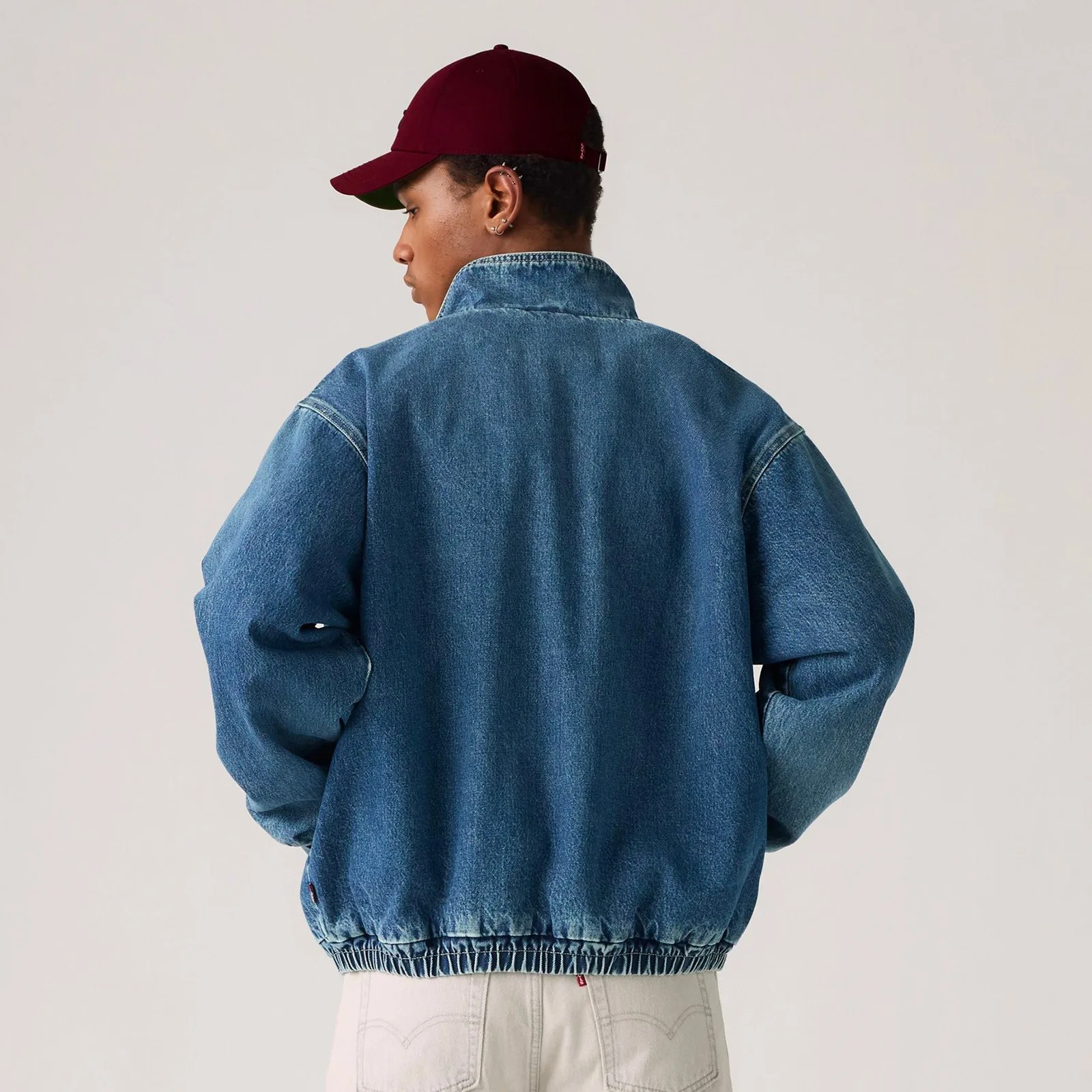 A male model is shown wearing the Levi's Highland Park Denim Jacket over a hooded sweatshirt showing the back of the jacket with his hands in his pocket