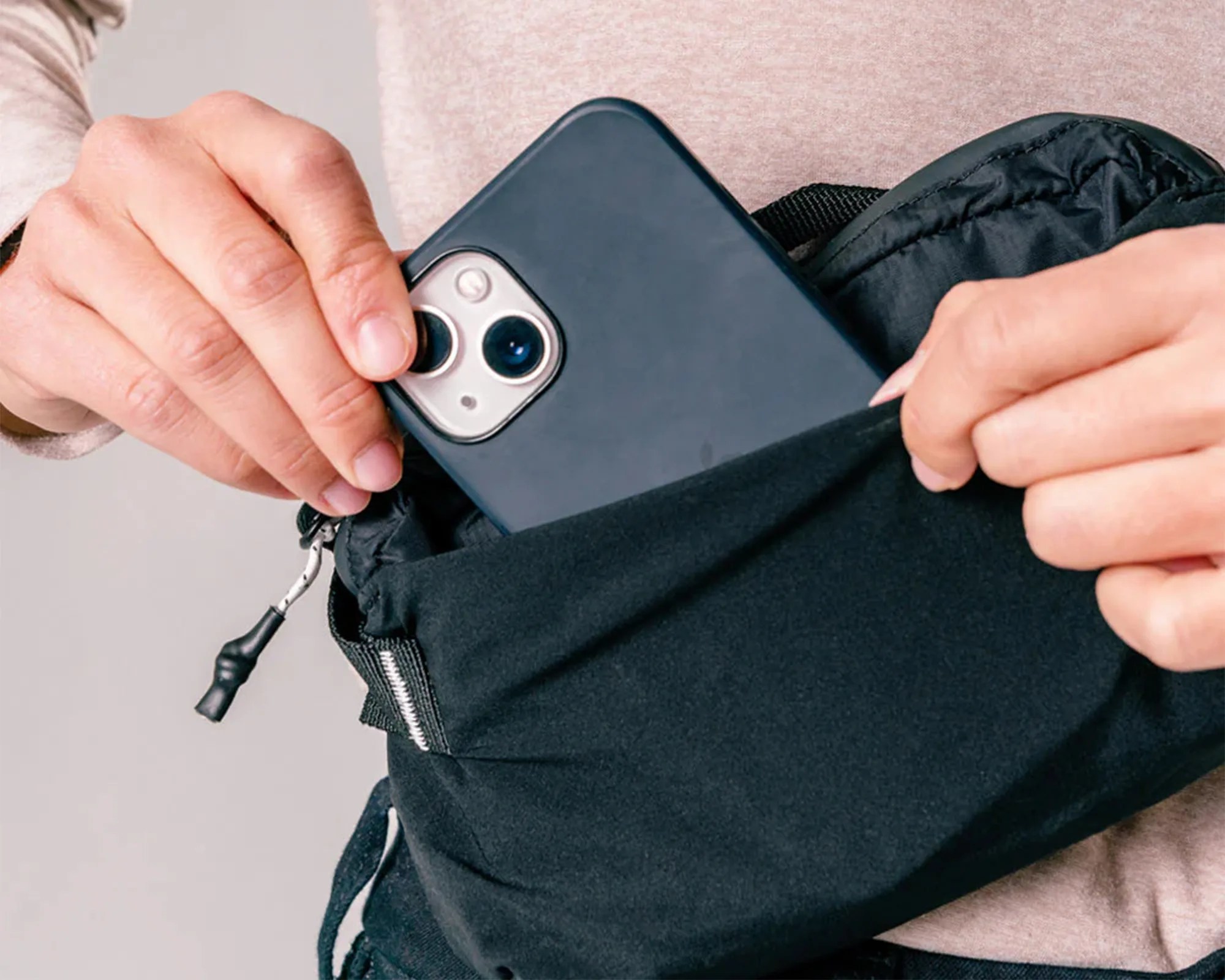 Person grabbing iPhone out of Matador ReFraction Packable Sling