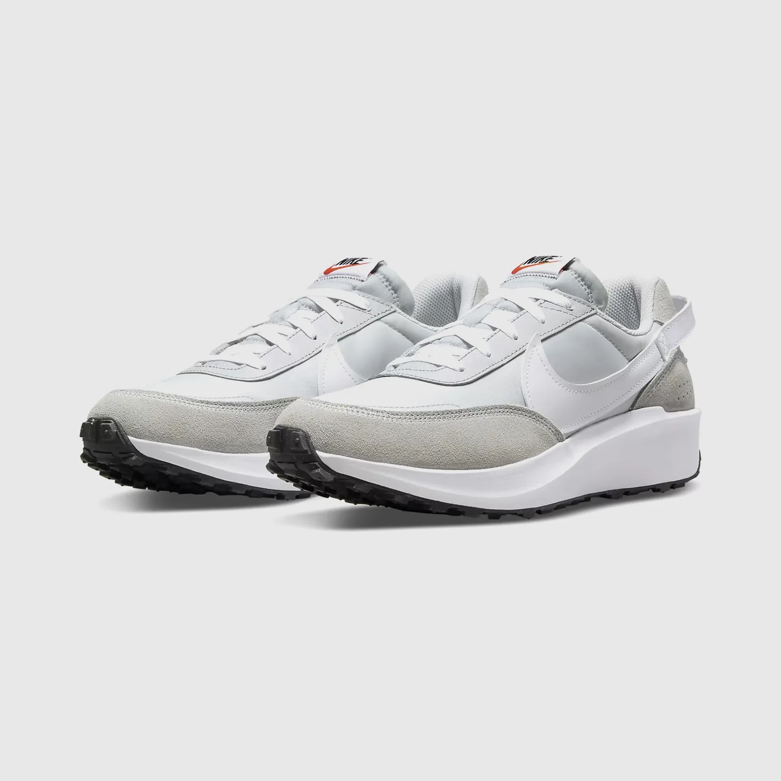 A pair of Nike Waffle Debut sneakers in white and grey shown at an angle