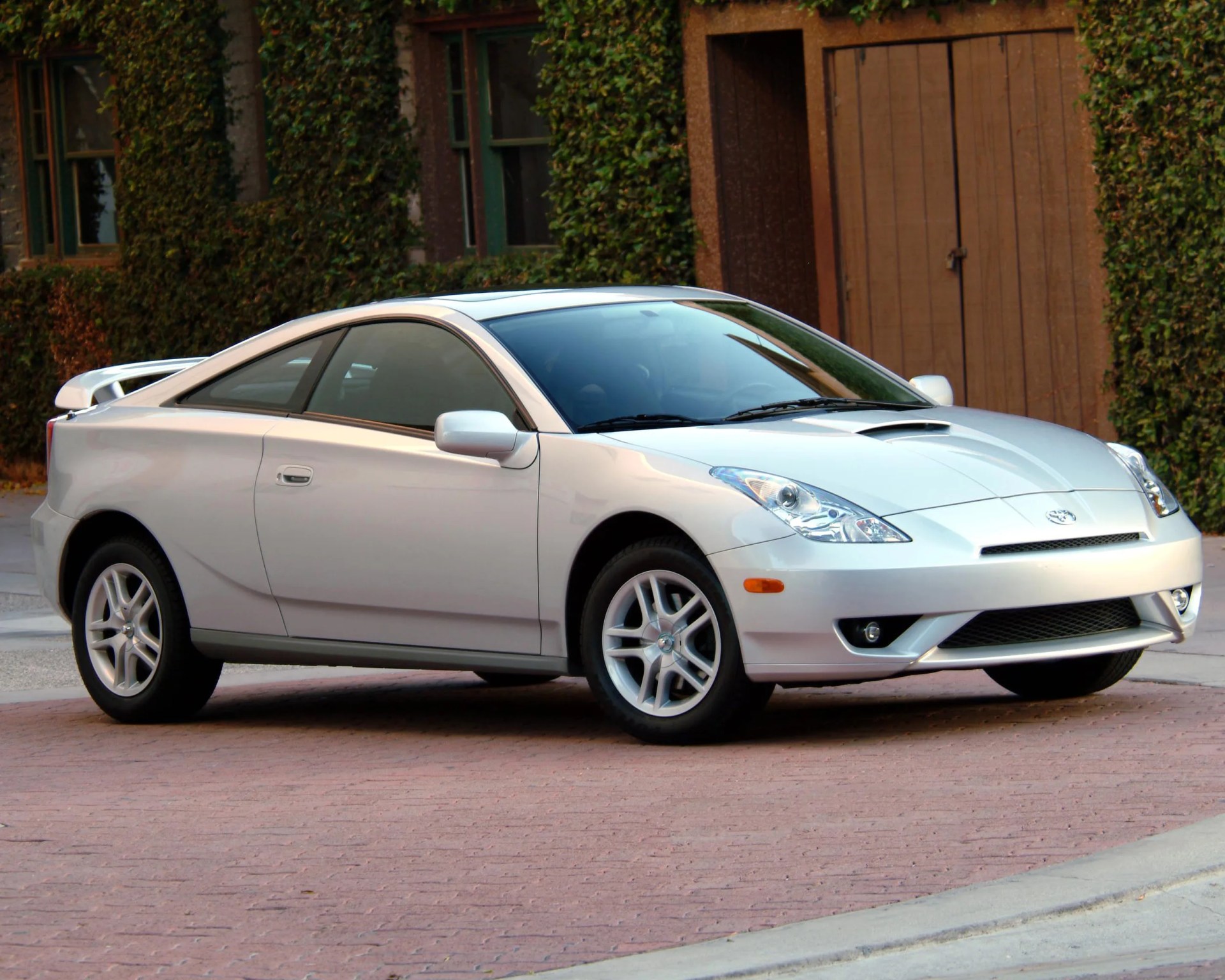 a photo showing a silver seventh-generation toyota celica parked in front of ivy
