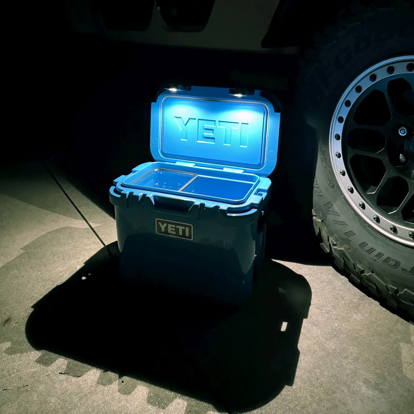 LatchOutdoors Latch Light shown illuminating a blue Yeti Roadie cooler at night, sitting next to a truck tire