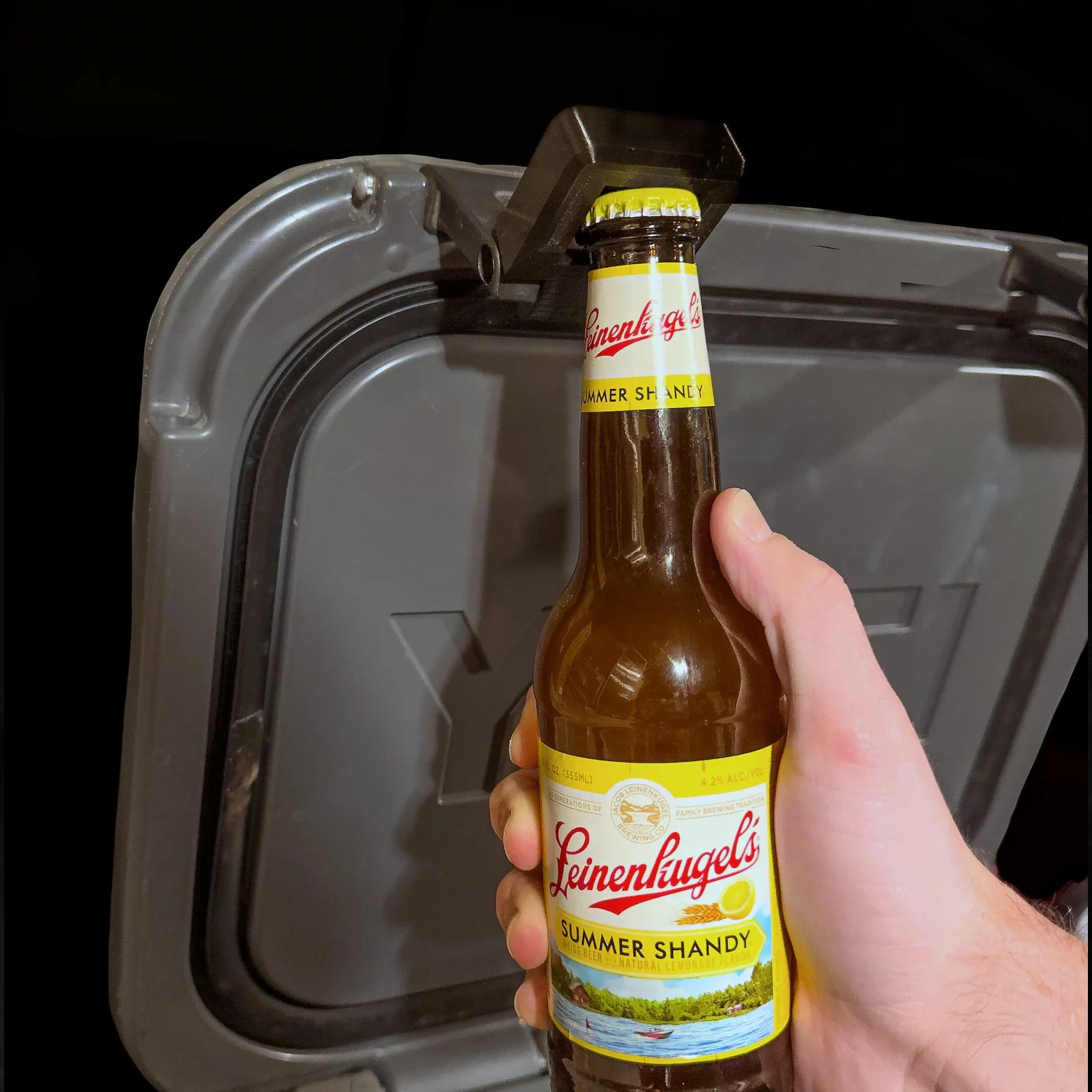 The LatchOutdoors Open Latch shown attached to a grey Yeti cooler and being used to open a glass beer bottle