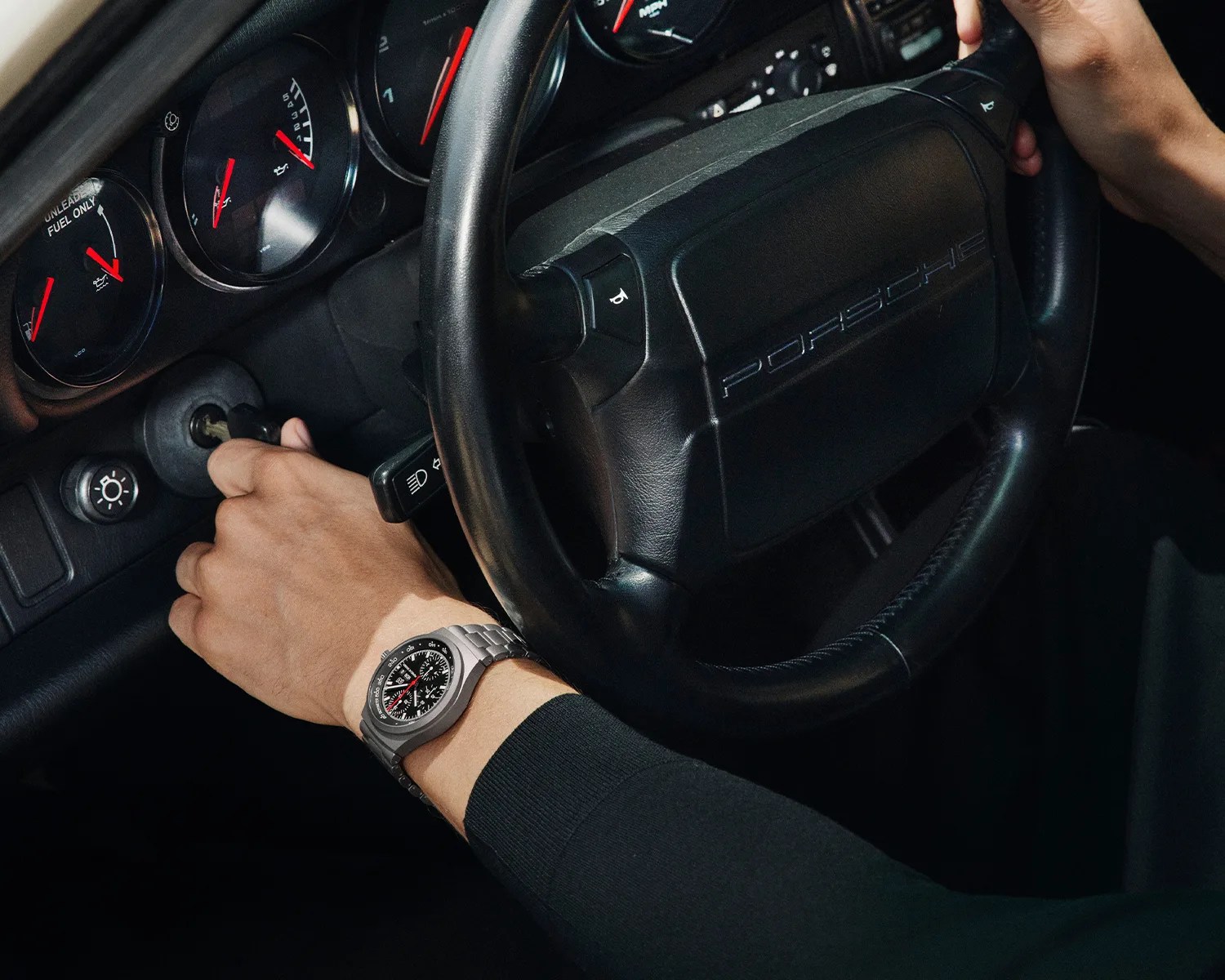 a porsche design chronograph watch on the wrist of a man starting a porsche car