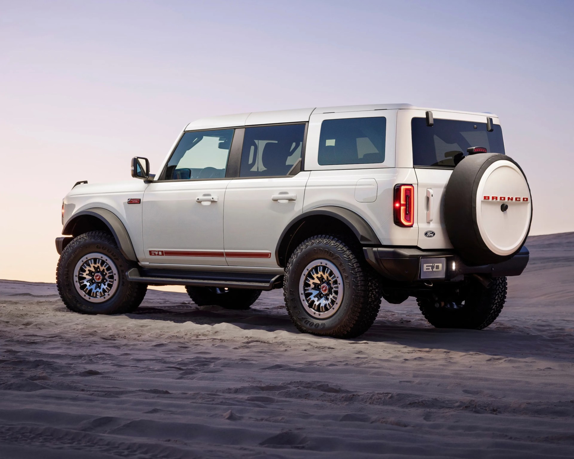 a photo of a white ford bronco suv on a sandy backdrop from the rear