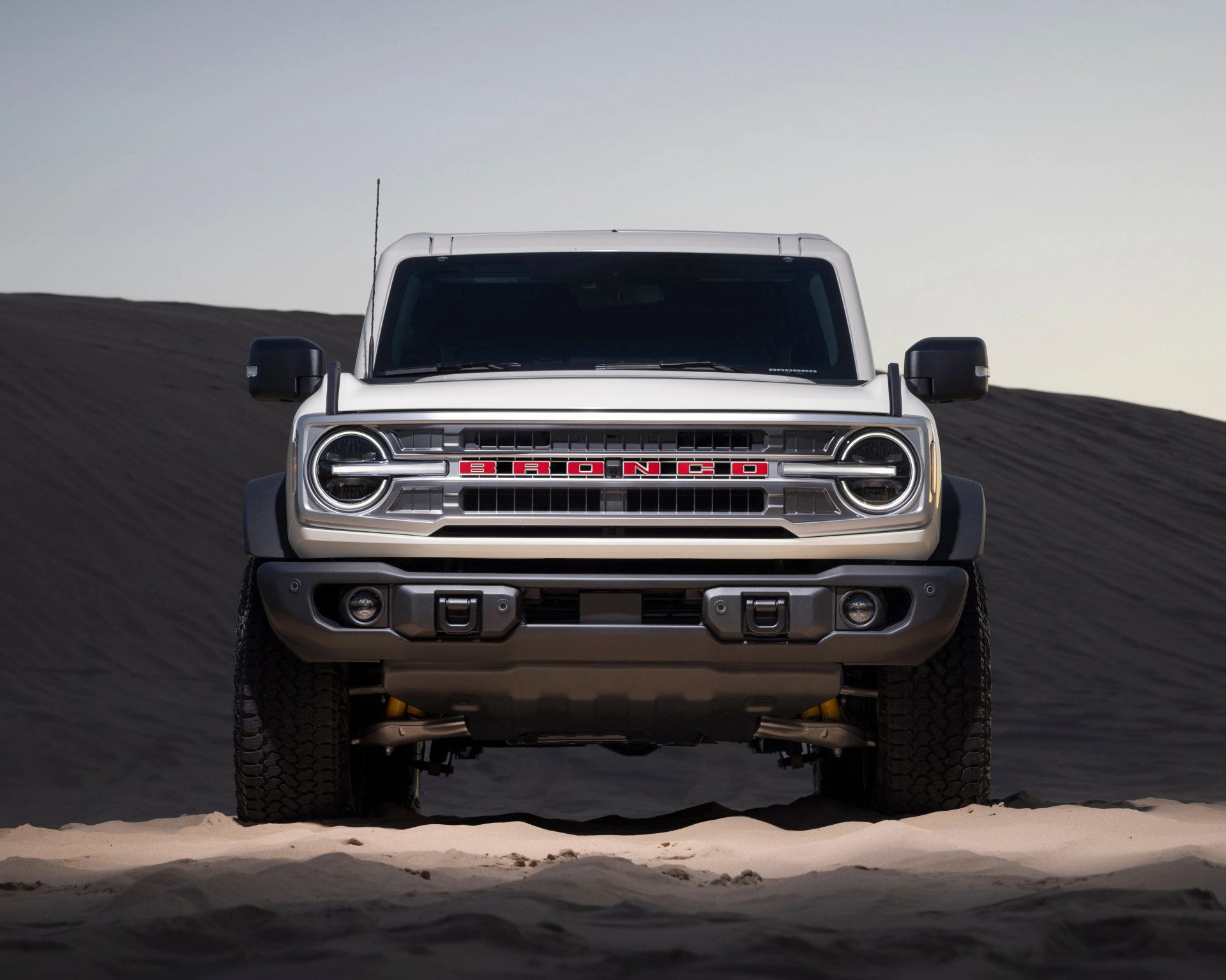 a photo of a white ford bronco suv on a sandy backdrop front-on