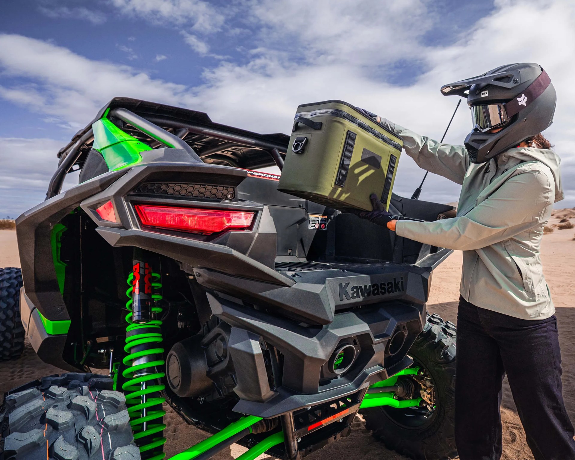 a photo of a woman wearing a dirt helmet loading a cooler into a side-by-side