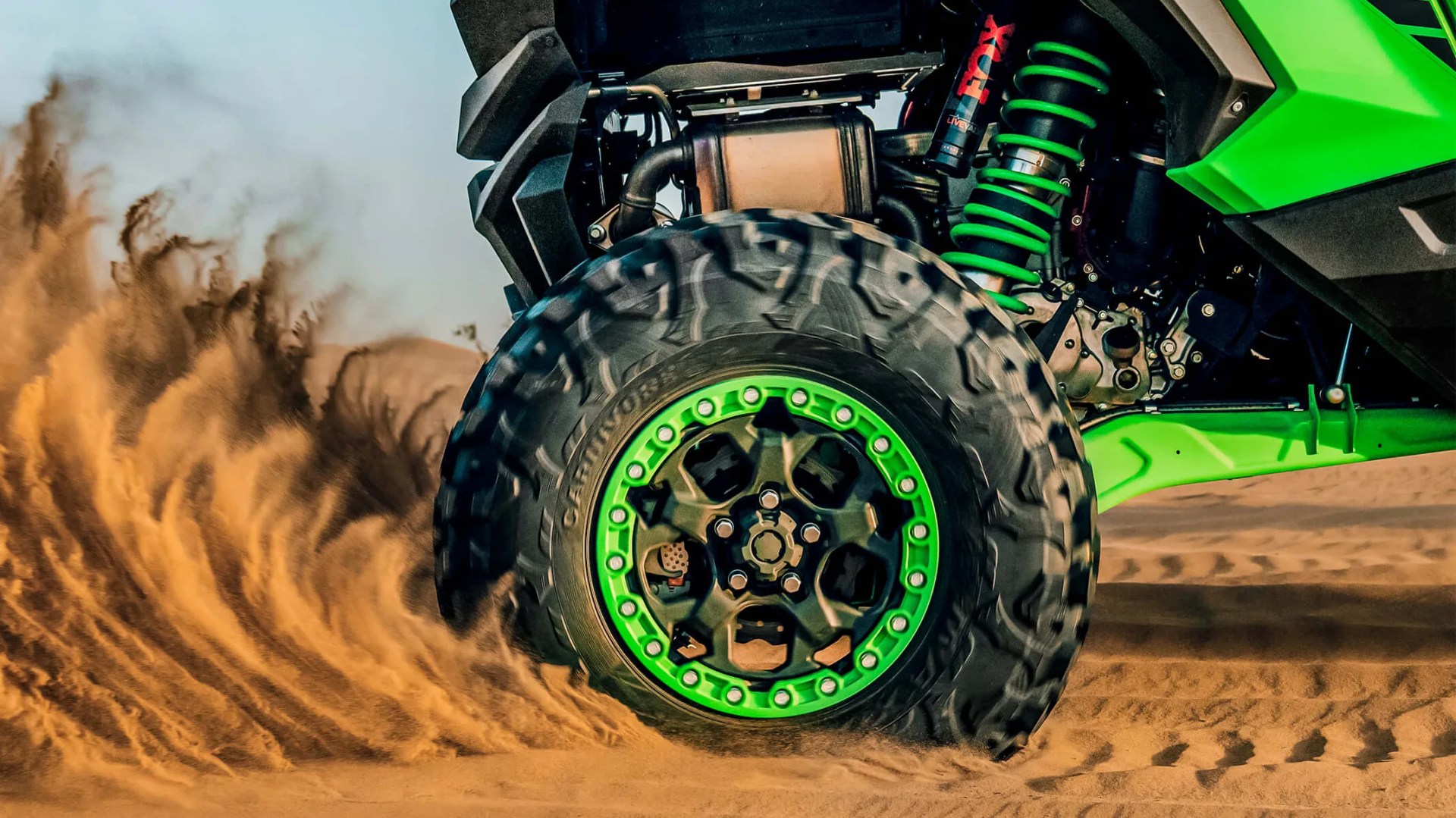a photo of a kawasaki UTV wheel kicking up sand