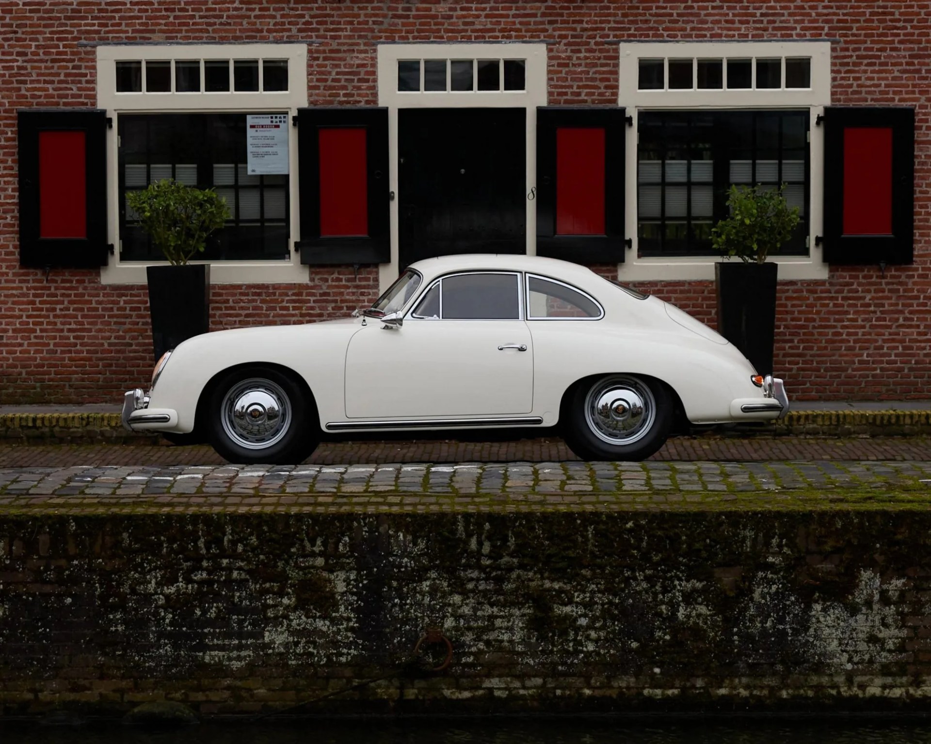 a photo of a classic porsche sports car parked in front of a brick building